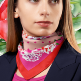 Woman wearing a colourful floral scarf with a pink and red design against a green leafy background