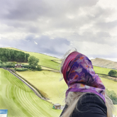 Person wearing a colourful Floral - dotted purple headscarf overlooking green fields and hills on a cloudy day.
