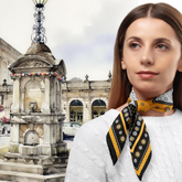 Woman wearing a patterned scarf in front of a fountain and building