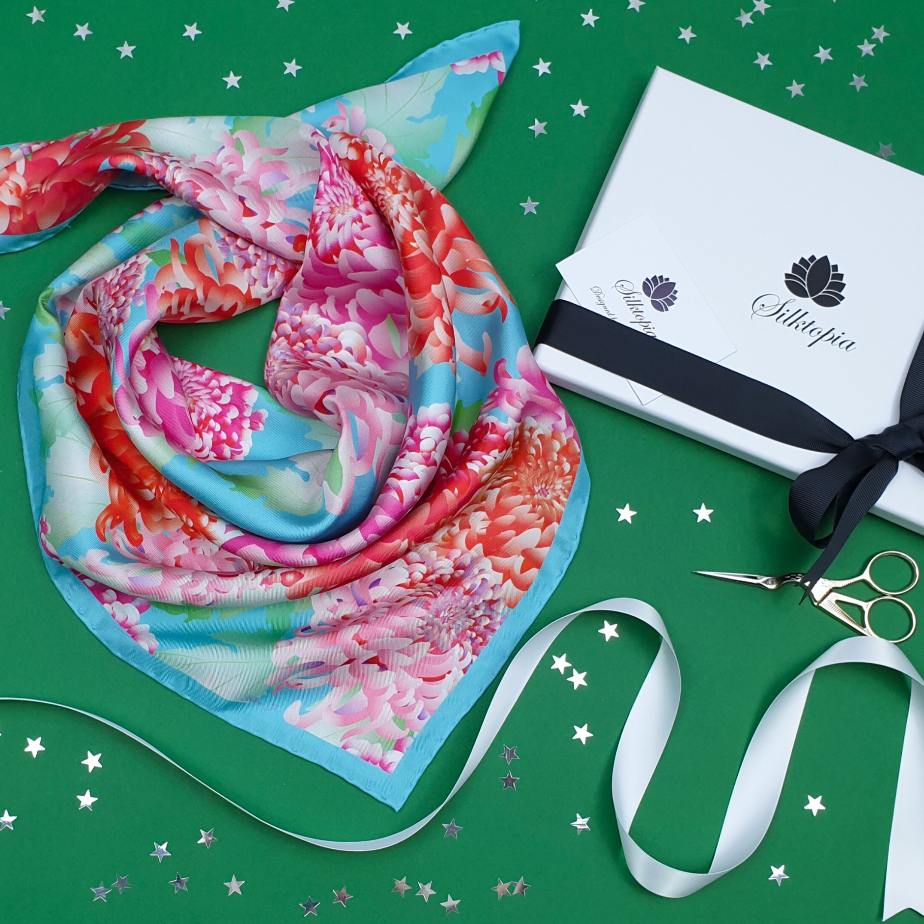 Colorful floral scarf with a white box, ribbon, and scissors on a green background