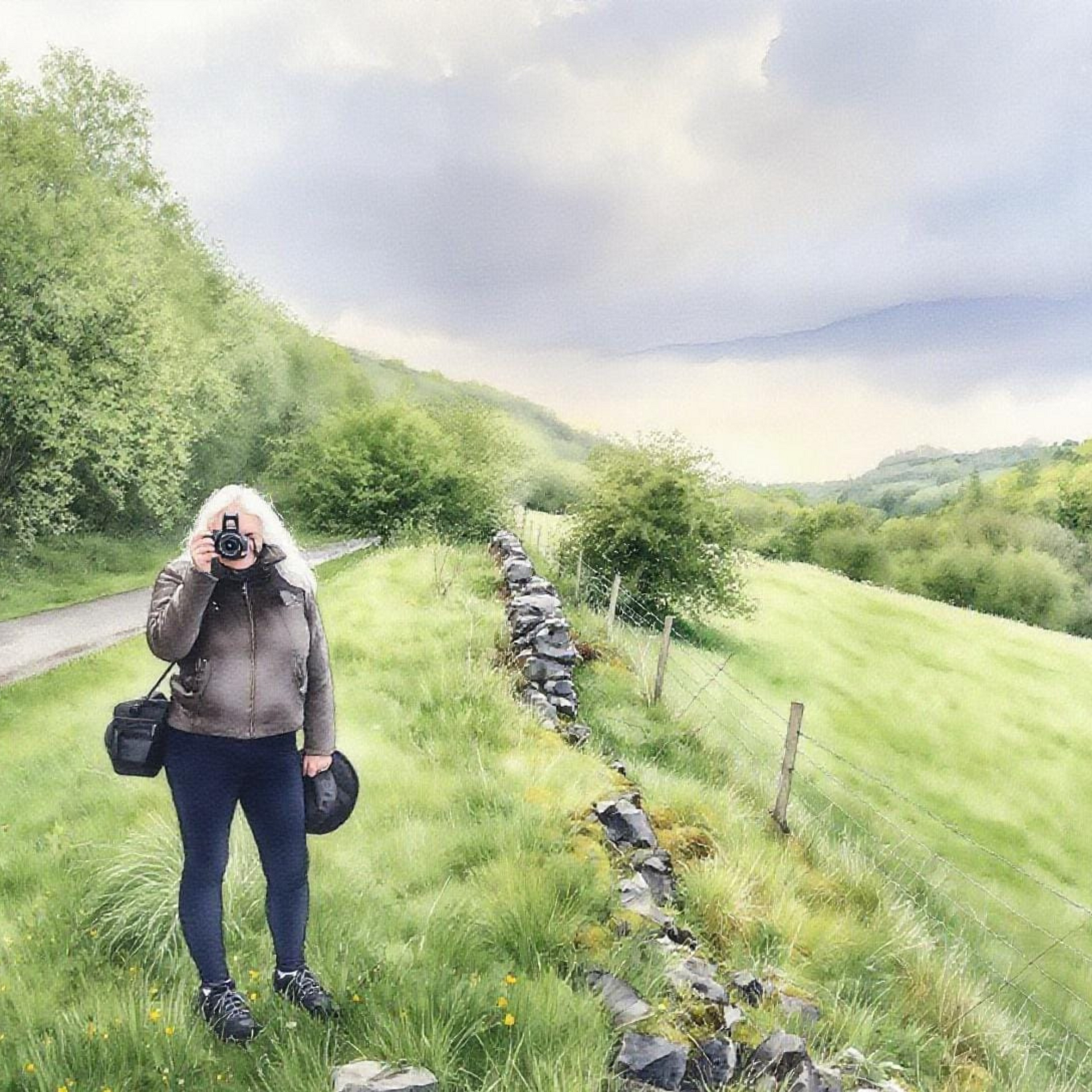 Person taking a photo in a scenic rural area with green fields and trees.